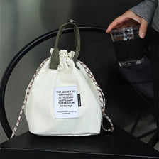 A white waterproof insulated lunch bag with a drawstring is held by a hand, resting on a black surface.