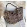 A leopard print canvas crossbody tote bag with a light brown and black pattern resting on a white surface.