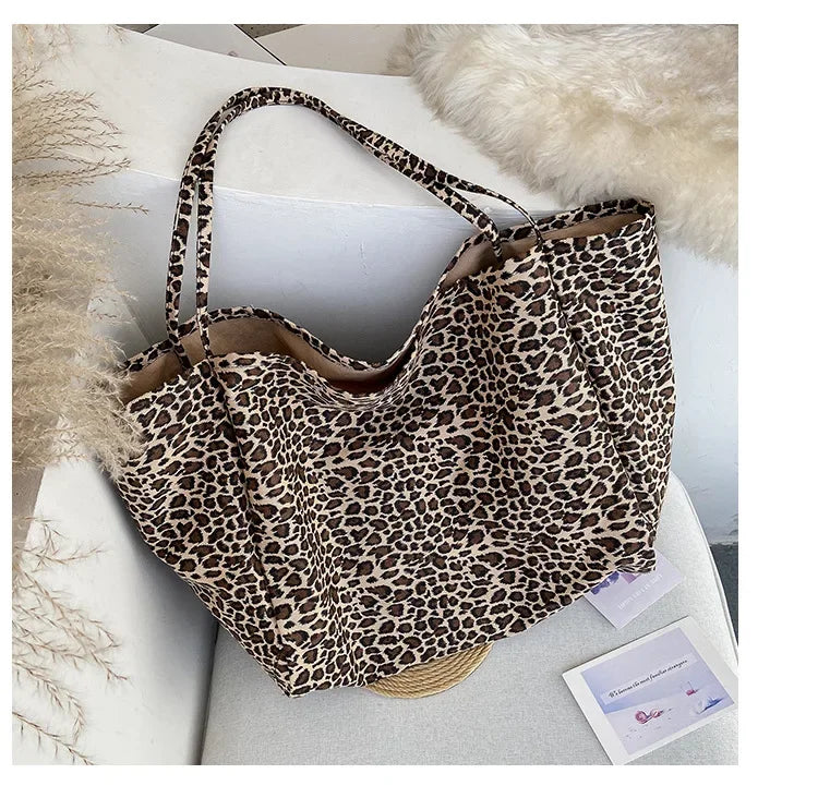 A leopard print canvas crossbody tote bag with a light brown and black pattern resting on a white surface.