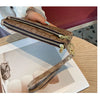 A brown textured zippered wallet with a gold-toned strap is shown being held by a hand on a wooden surface.