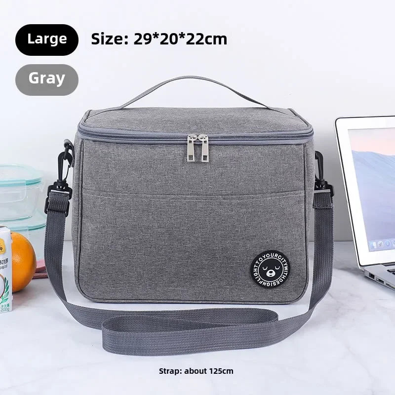 A gray insulated portable lunch bag with a shoulder strap is shown on a white surface.