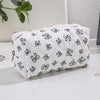 Bolsa de maquillaje blanca con estampado de lazo negro sobre una superficie blanca.