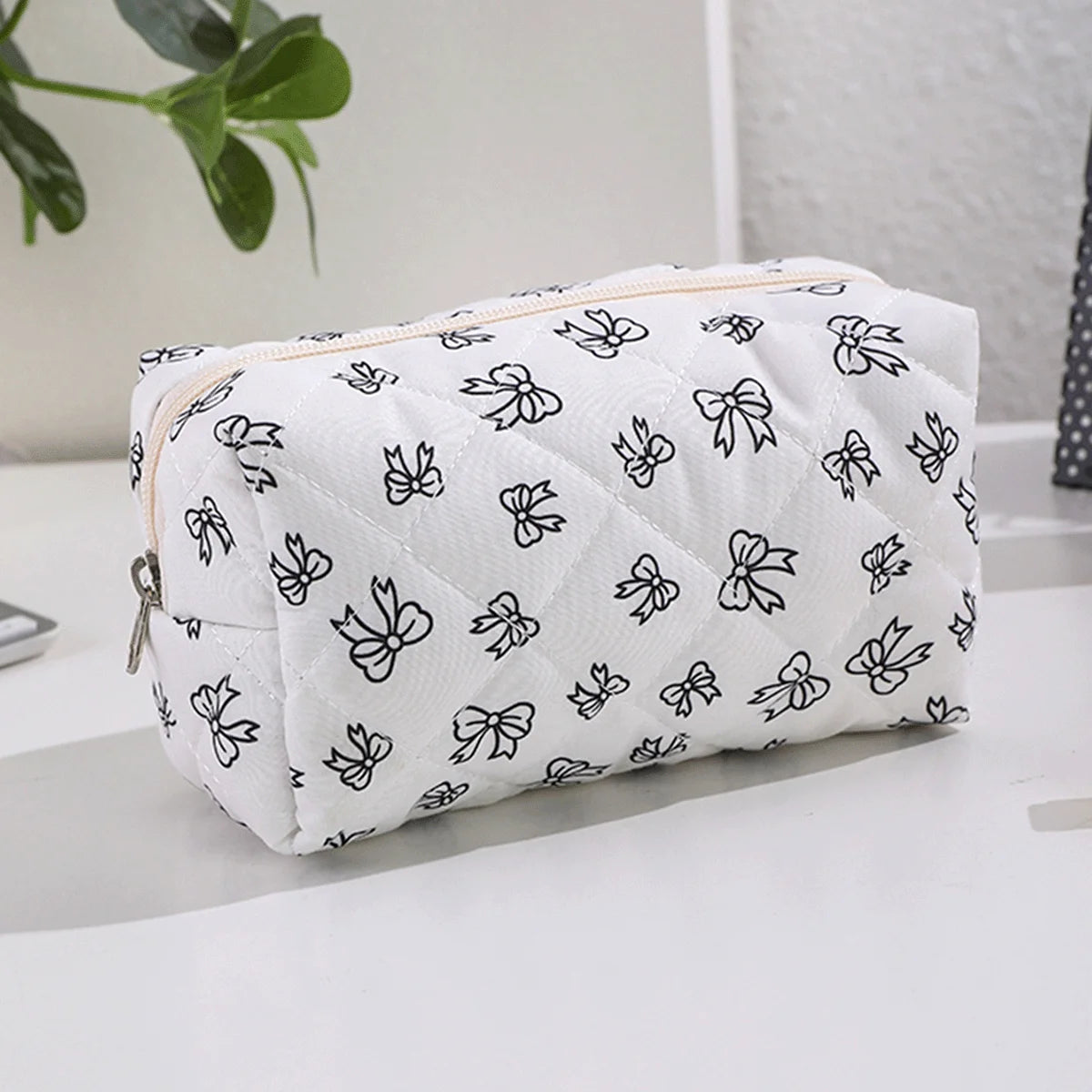 Bolsa de maquillaje blanca con estampado de lazo negro sobre una superficie blanca.