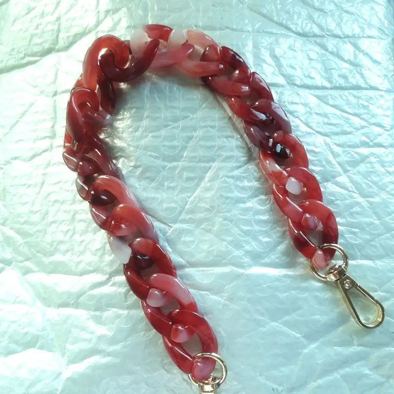 A close-up of a reddish-pink multicolor acrylic chain bracelet on a white background.