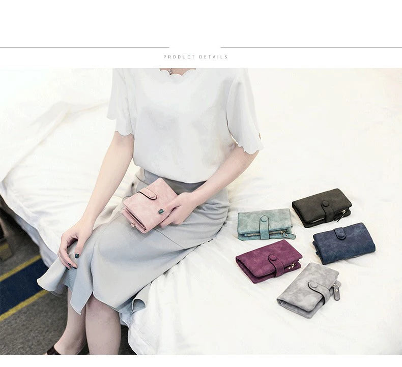 A woman wearing a light gray top and skirt is sitting on a white bed, holding several multi-slot card wallets.