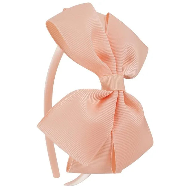 A light peach colored ribbon bow headband shown from the side.