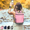 A woman is using her phone to take a picture while wearing a pink cooler backpack outdoors.