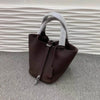 Dunkelbraunes Leder-Bucket-Bag mit hellem grauem Stoffgriff auf grauem Untergrund.