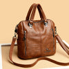 A brown leather fashionable crossbody backpack bag with silver hardware shown against a light background.