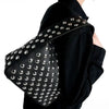A black leather shoulder bag adorned with silver metal rivets and studs, worn over a black jacket.