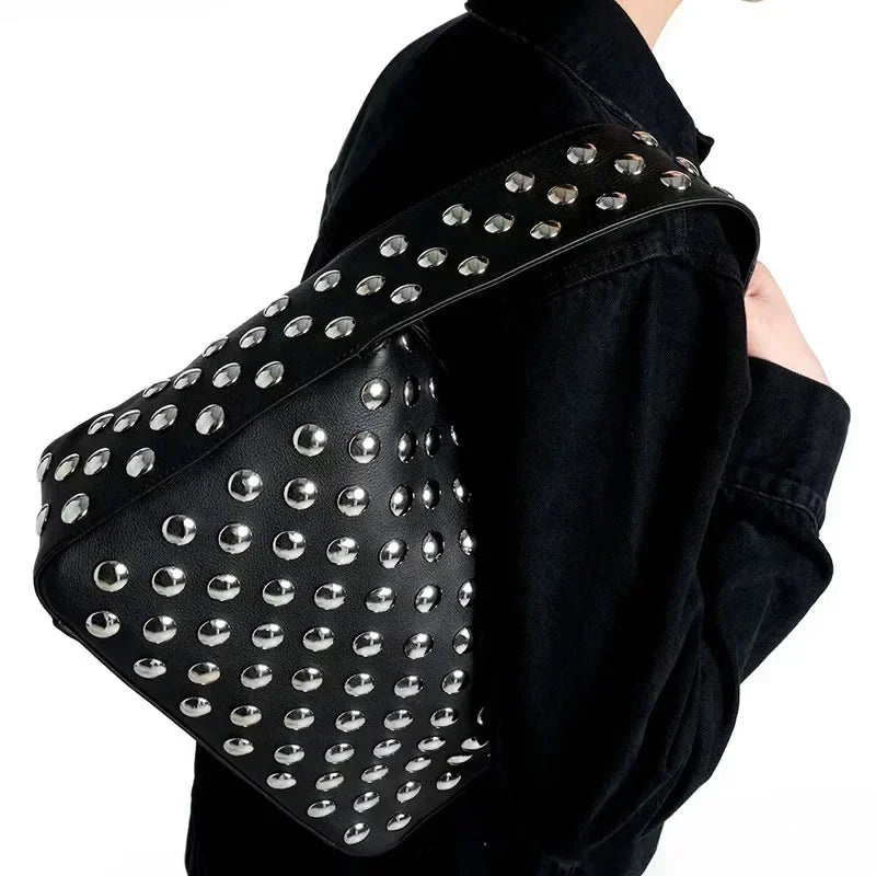 A black leather shoulder bag adorned with silver metal rivets and studs, worn over a black jacket.