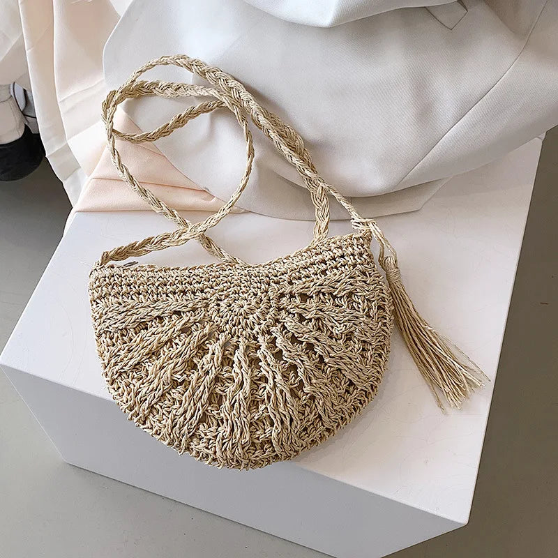 A beige handmade rattan straw crossbody bag resting on a white box with draped fabric.