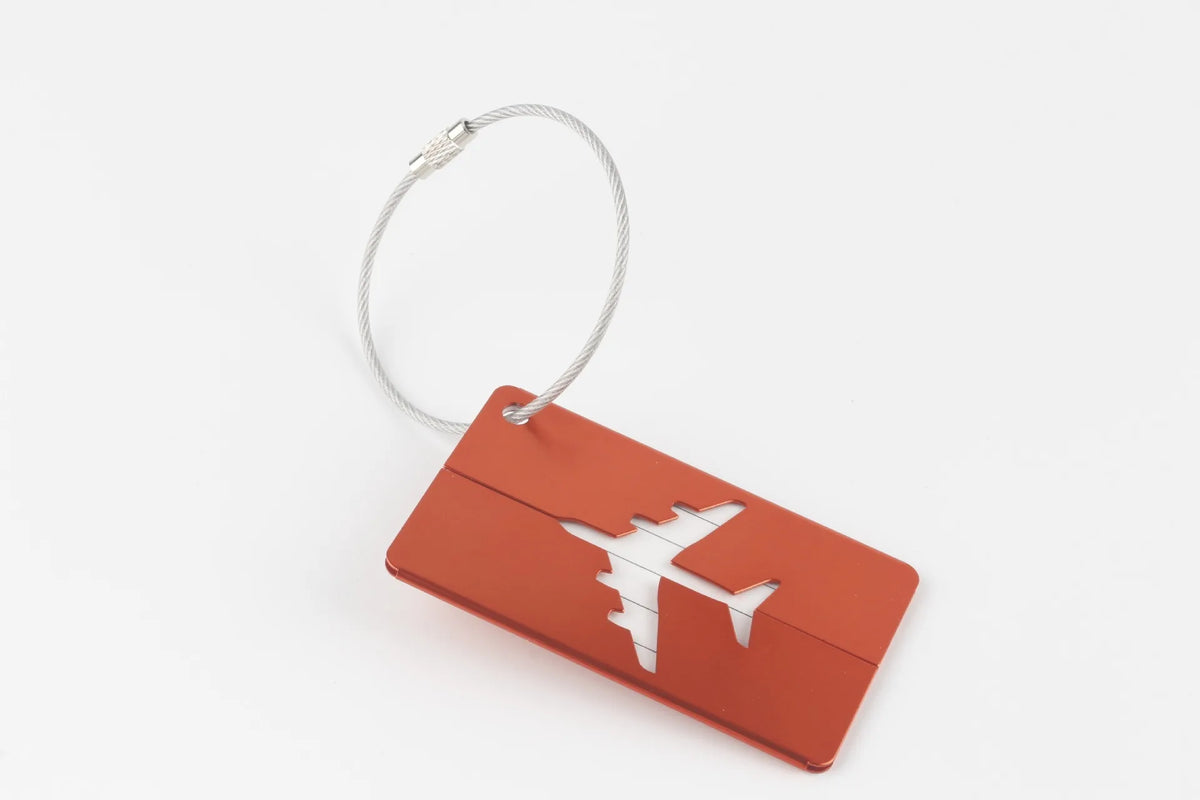A rectangular orange luggage tag with a silver loop attached, featuring a white airplane silhouette.
