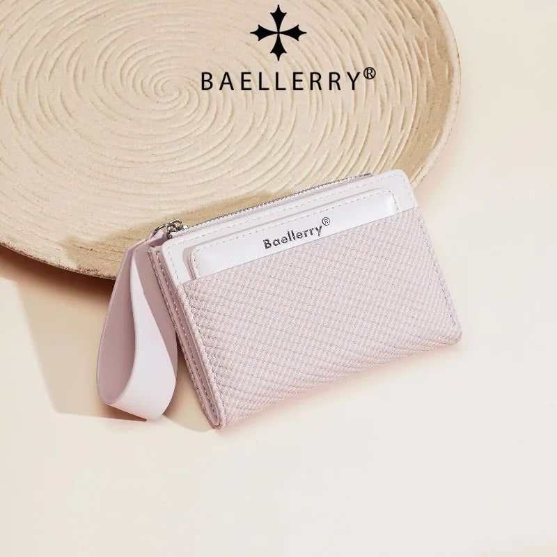 A light pink Baellery zip-around wallet with a white leather flap resting on a beige woven mat.