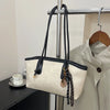 A beige classic PU leather tote bag with black leather straps and gold hardware hanging on a metal rack.