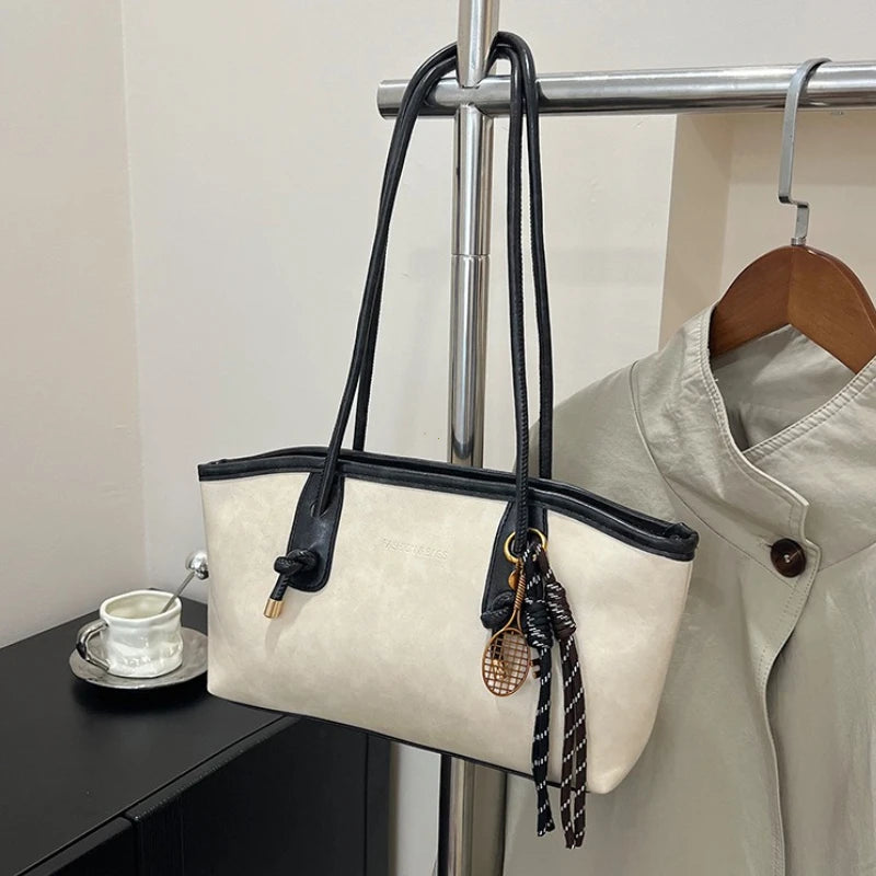 A beige classic PU leather tote bag with black leather straps and gold hardware hanging on a metal rack.