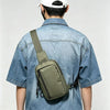 A person wearing a denim shirt is holding a olive green chest bag on their back.