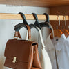 Eine braune Lederhandtasche hängt an einem Klebeflansch in einem Holzschrank neben anderen Taschen und Haken.