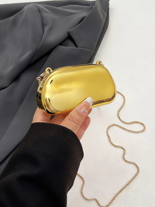 A hand holds a mini gold metal clutch bag against a dark gray fabric background.