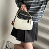 A woman holds a cream-colored shoulder bag with a gold chain and black leather accents, paired with a striped top and black s