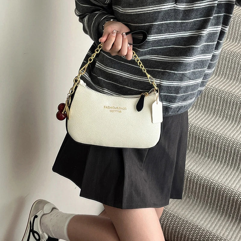 A woman holds a cream-colored shoulder bag with a gold chain and black leather accents, paired with a striped top and black s