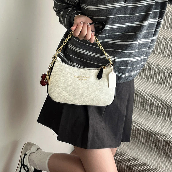 A woman holds a cream-colored shoulder bag with a gold chain and black leather accents, paired with a striped top and black s