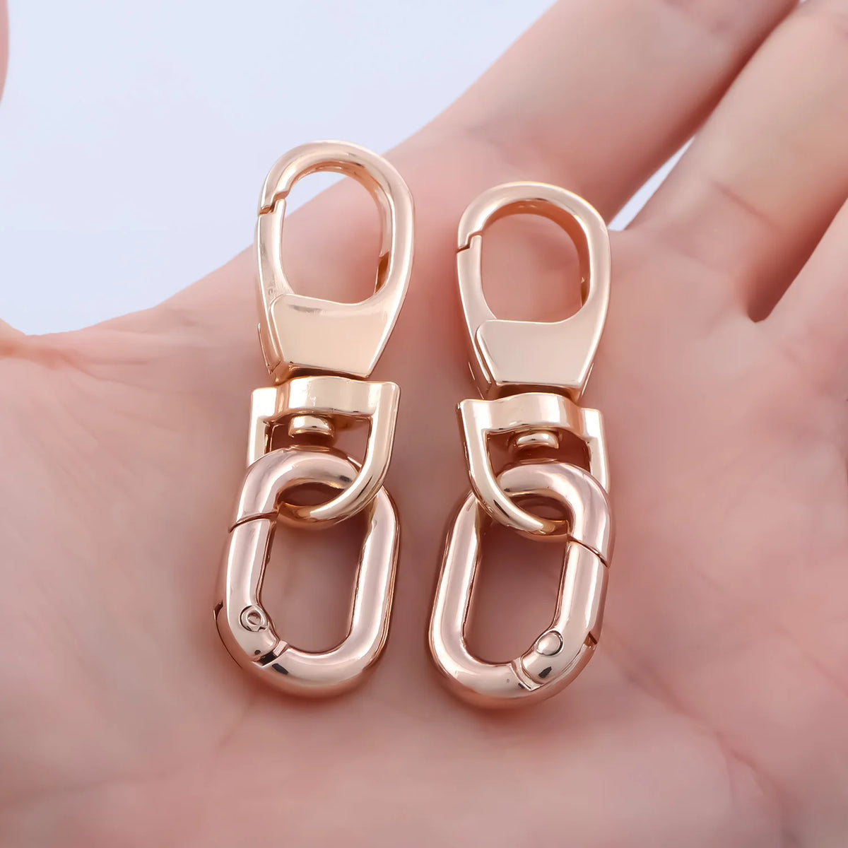 Pair of gold-toned metal swivel lobster claw clasps with key rings shown on a hand.