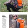 Une femme portant une veste beige est assise à l'extérieur avec un sac à dos d'escalade imperméable orange et gris.