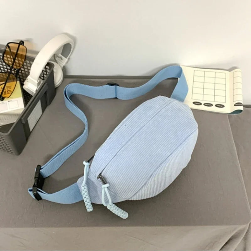 Light blue corduroy waist pack for women displayed on a gray surface next to headphones and a notebook.