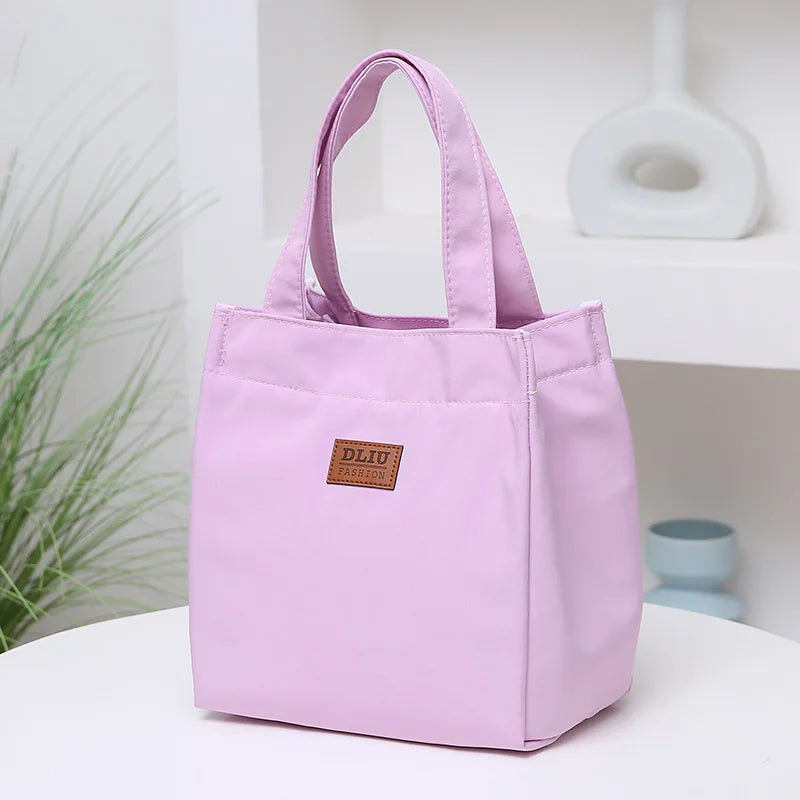 A light purple durable aluminum foil insulated lunch bag with handles resting on a white shelf.