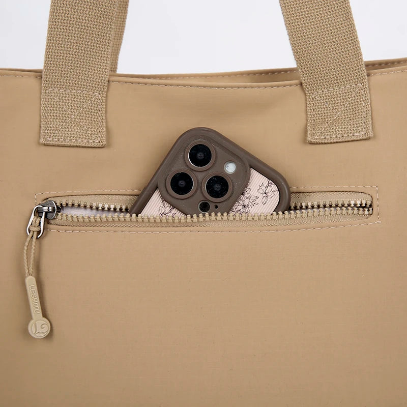 A beige canvas tote bag with tan straps and a zippered pocket featuring a phone holder.