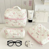 Sac de rangement cosmétique rembourré blanc avec motif nœud rose, à côté de lunettes de soleil et d'un petit animal en peluch