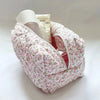 Bolsa de maquillaje acolchada con cremallera floral, patrón rosa y blanco, con una botella de plástico transparente dentro.
