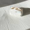 A white cotton toiletry pouch with a zipper is lying on a light striped fabric surface.