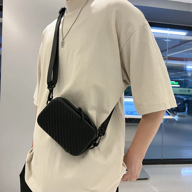 A person wearing a cream t-shirt displays a black striped PU leather shoulder bag hanging from the shirt.