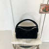 A black faux suede crossbody bag resting on a white knitted surface.