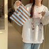 Una persona sostiene una bolsa de almacenamiento de lona a rayas con franjas marrón y azul claro contra una sudadera blanca.