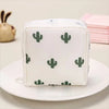 A white fabric pouch with a repeating green cactus pattern, resting on a white plate.