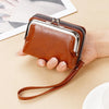 A brown vintage PU leather compact wallet with a silver zipper and leather strap is held in a hand.