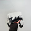 A white and black piano note embroidered crossbody bag is held by a person wearing a black sleeve.