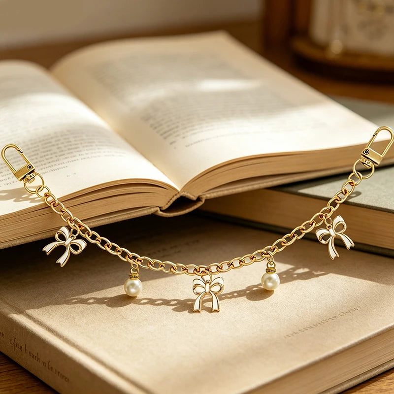 A gold chain necklace with pearl and bow charms rests on an open book.