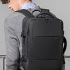 A man wearing a grey sweater is shown from the back, carrying a black men's business travel backpack.
