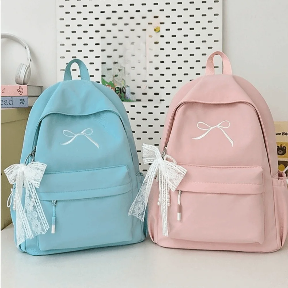 A light blue backpack and a pink backpack with white embroidery are displayed on a white surface.