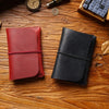A close-up of a red leather passport holder and a black leather card wallet resting on a wooden surface with a vintage clock 