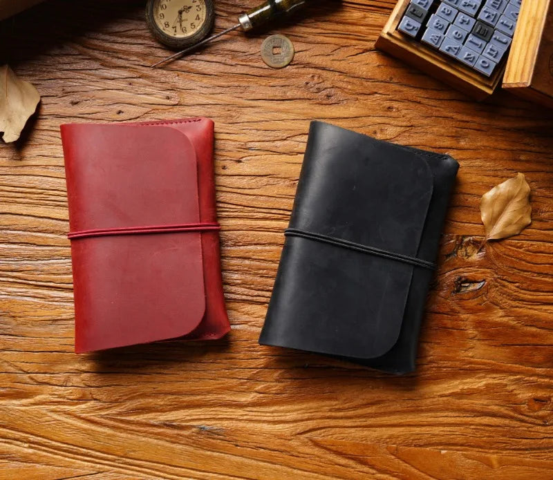 A close-up of a red leather passport holder and a black leather card wallet resting on a wooden surface with a vintage clock 