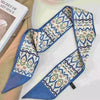 Foulard pour les cheveux en soie à motif bleu et crème drapé sur un fond clair.