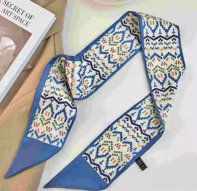 Foulard pour les cheveux en soie à motif bleu et crème drapé sur un fond clair.