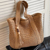 A natural straw woven tote bag with a brown leather strap resting on a dark surface.