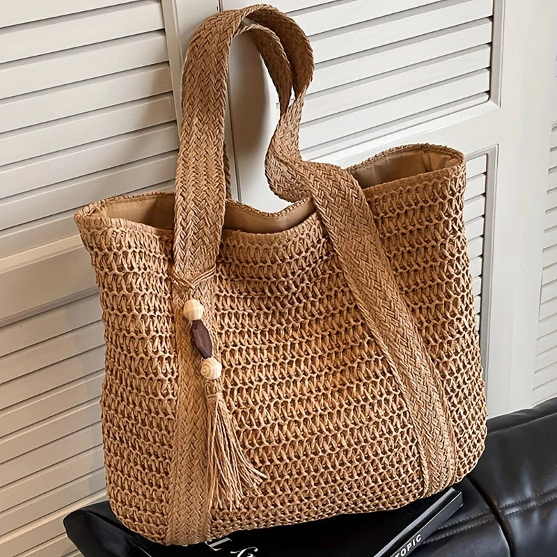 A natural straw woven tote bag with a brown leather strap resting on a dark surface.