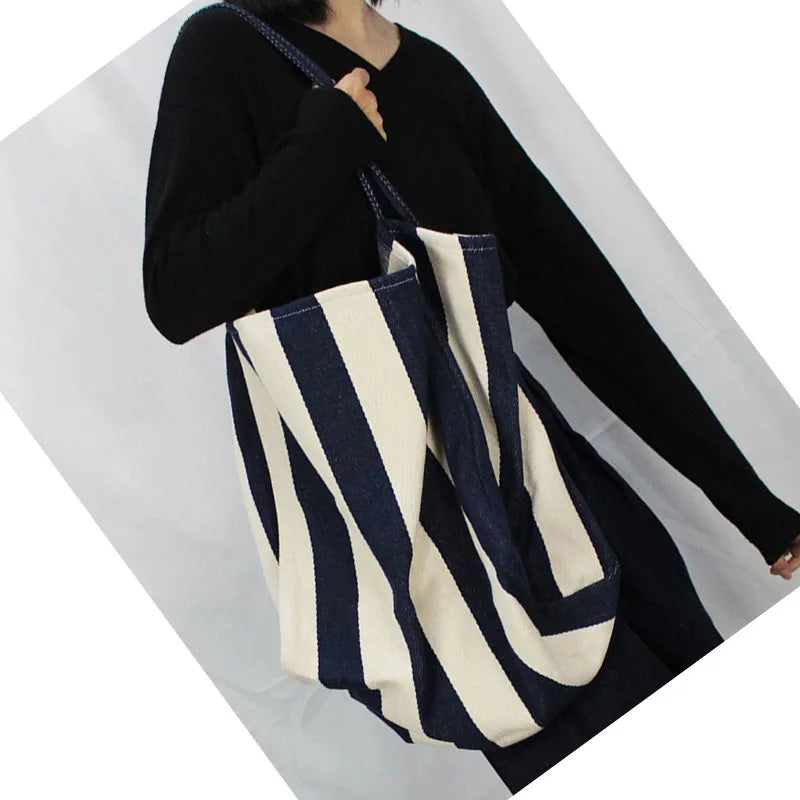A person holds a striped canvas tote bag with an inner pocket against a white background.